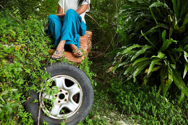 woman sitting on tyre in forest wearing our sandals made out of recycled materials. 