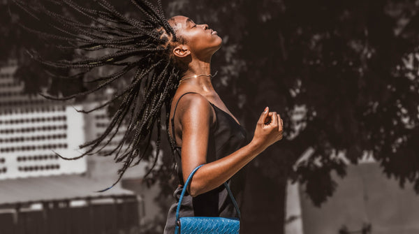   a women flipping her hair back and holding the blue crossbody bag.