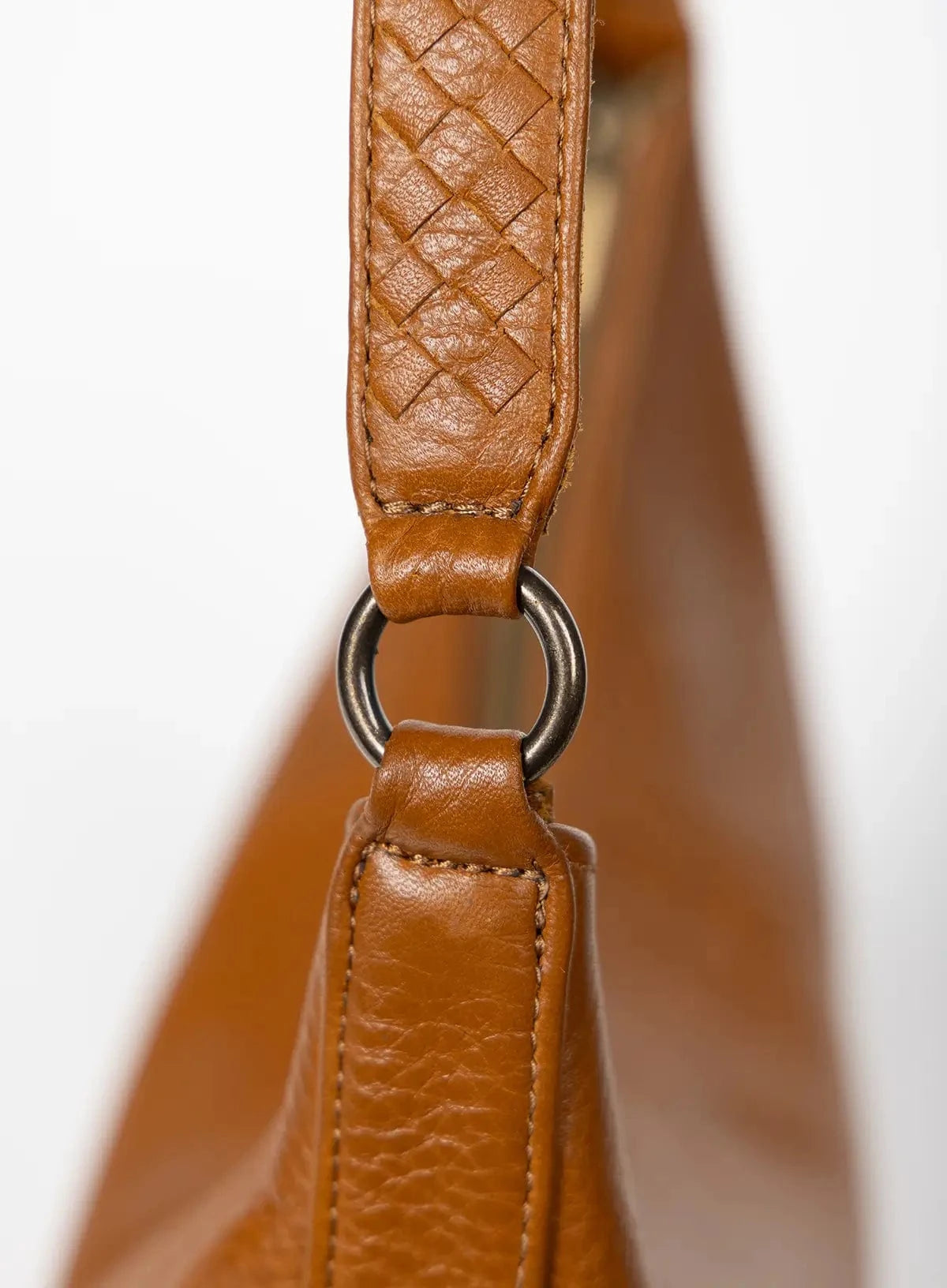Close-up of a honey leather handbag handle with braided design.
