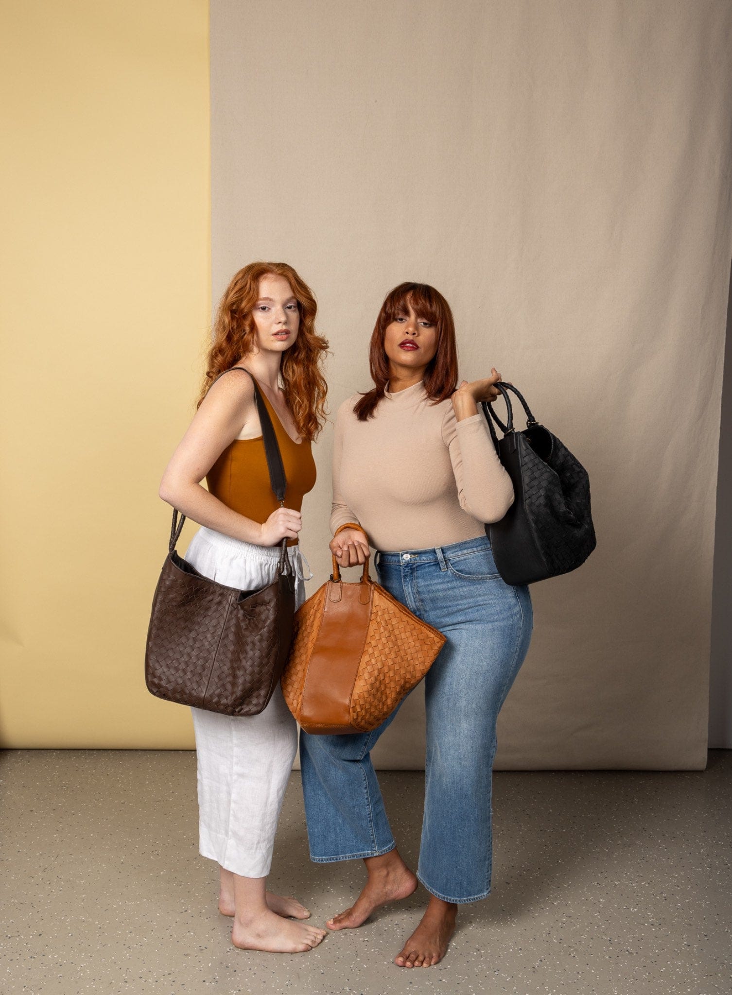 Two women holding handbags against a neutral background