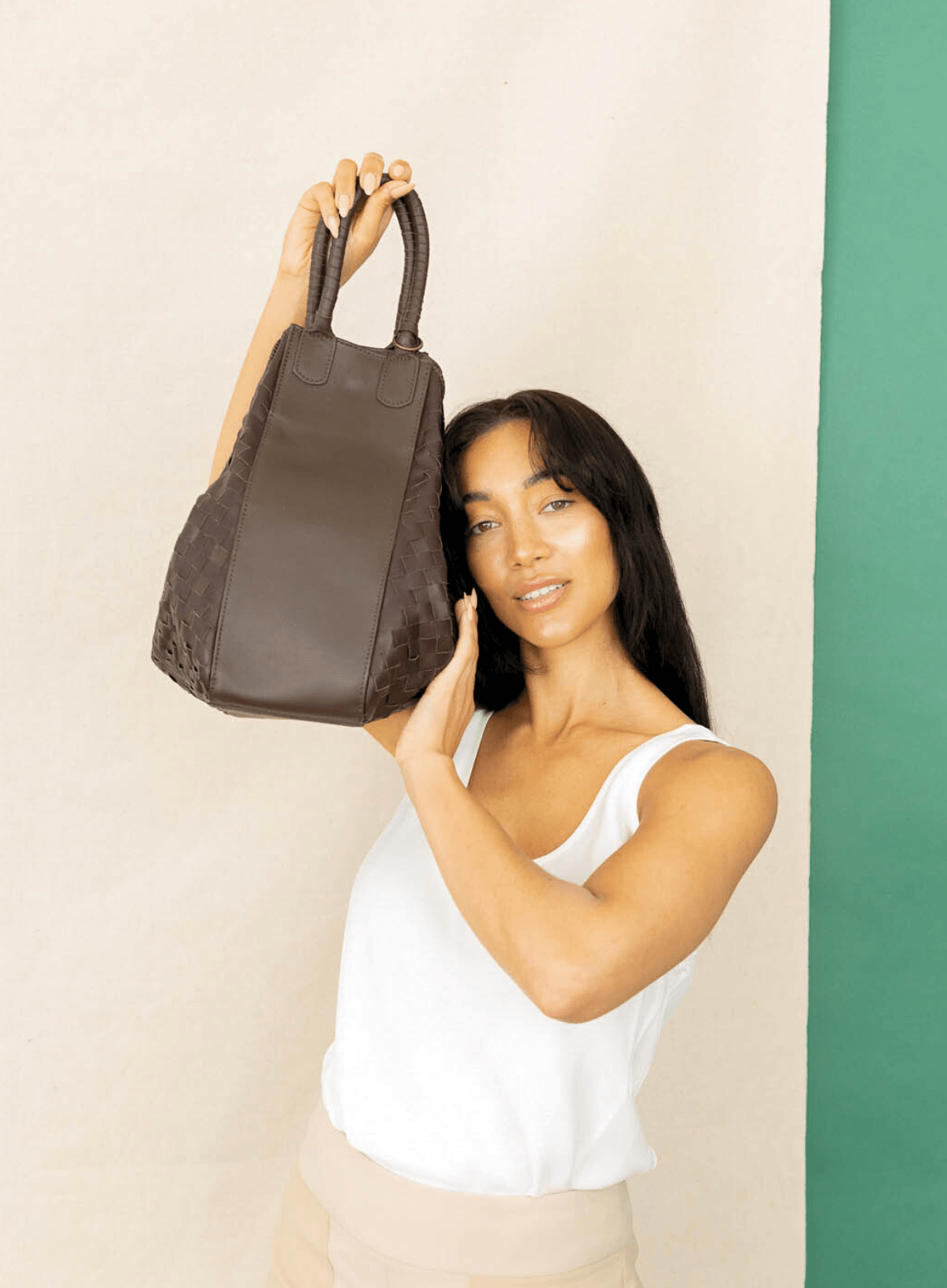 Woman holding a brown leather handbag against a beige and green background