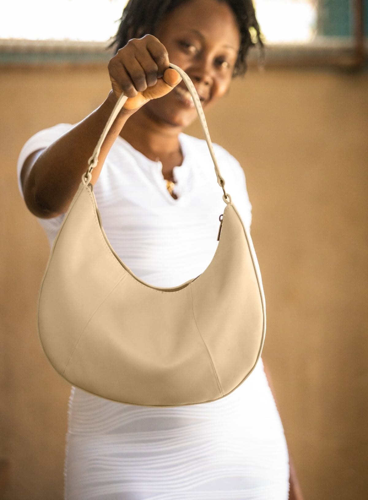 Woman holding a beige handbag against a neutral background
