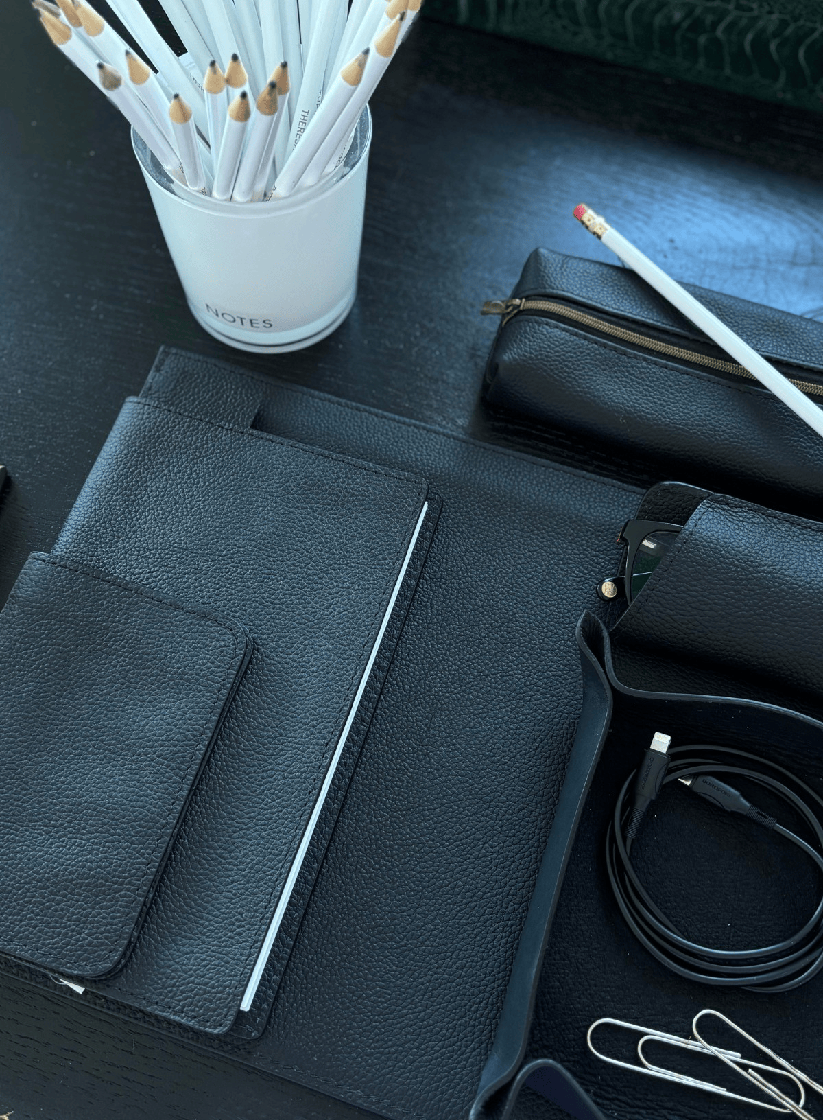 Black leather pouch with stationery items on a dark surface