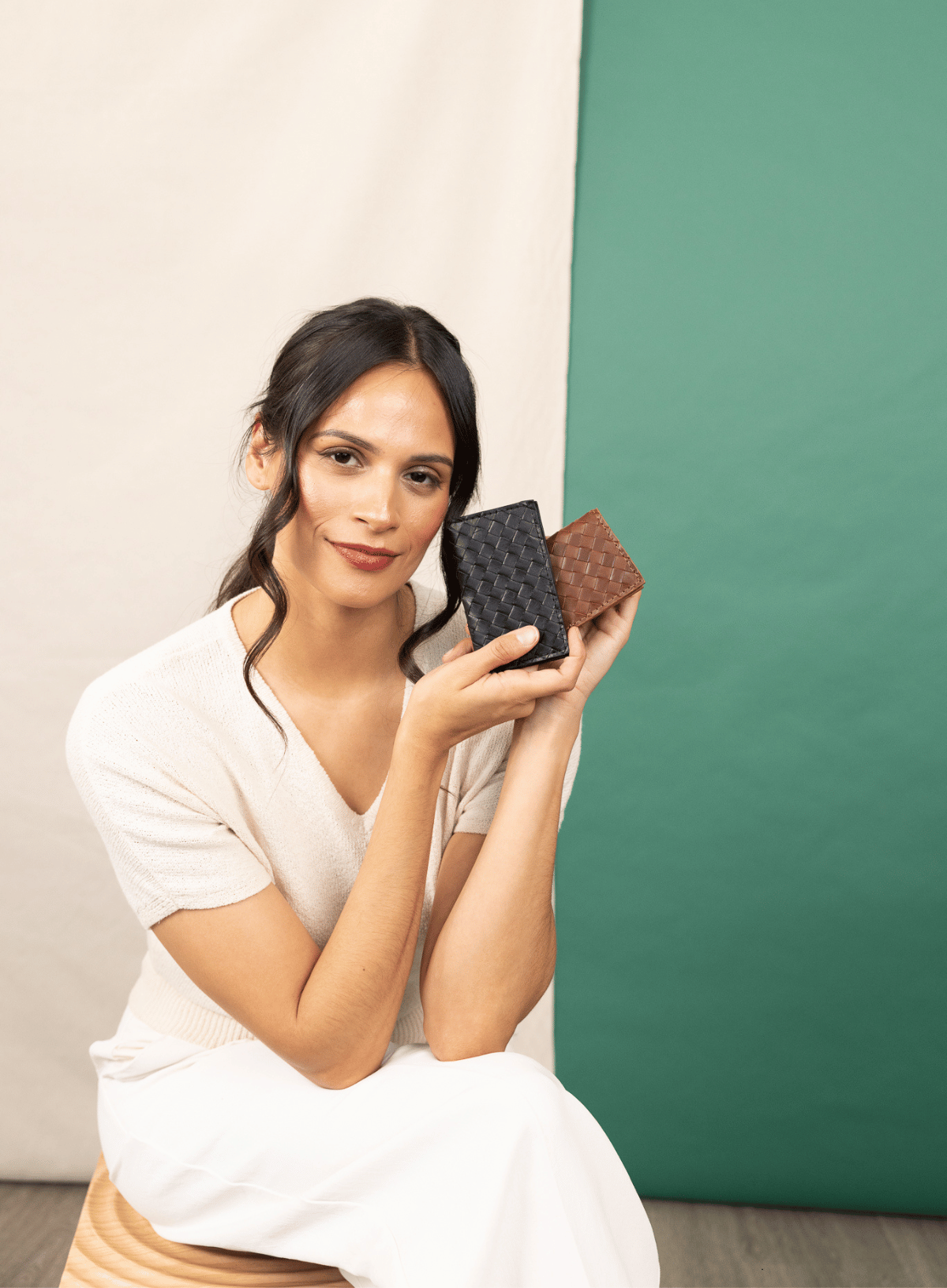 woman holding woven wallets in front of green and white backgrounds