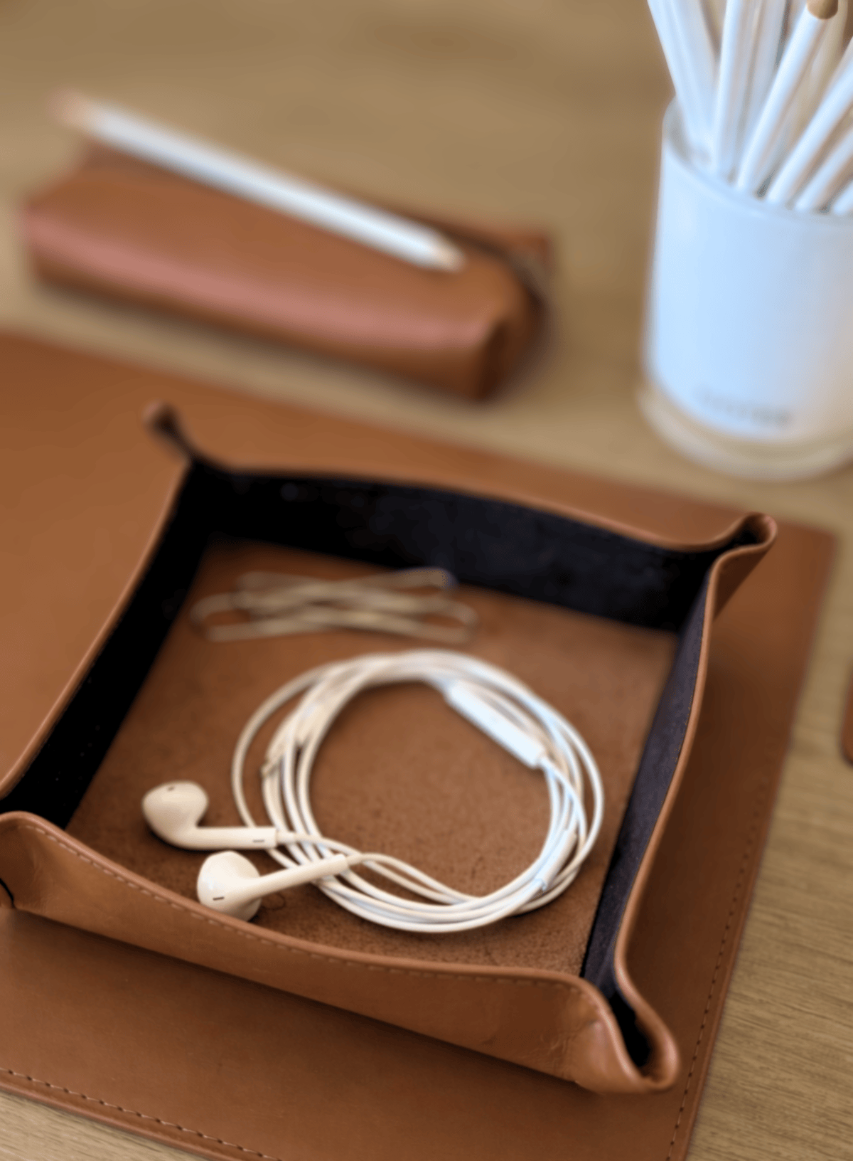 Cognac leather case with white earbuds on a wooden surface