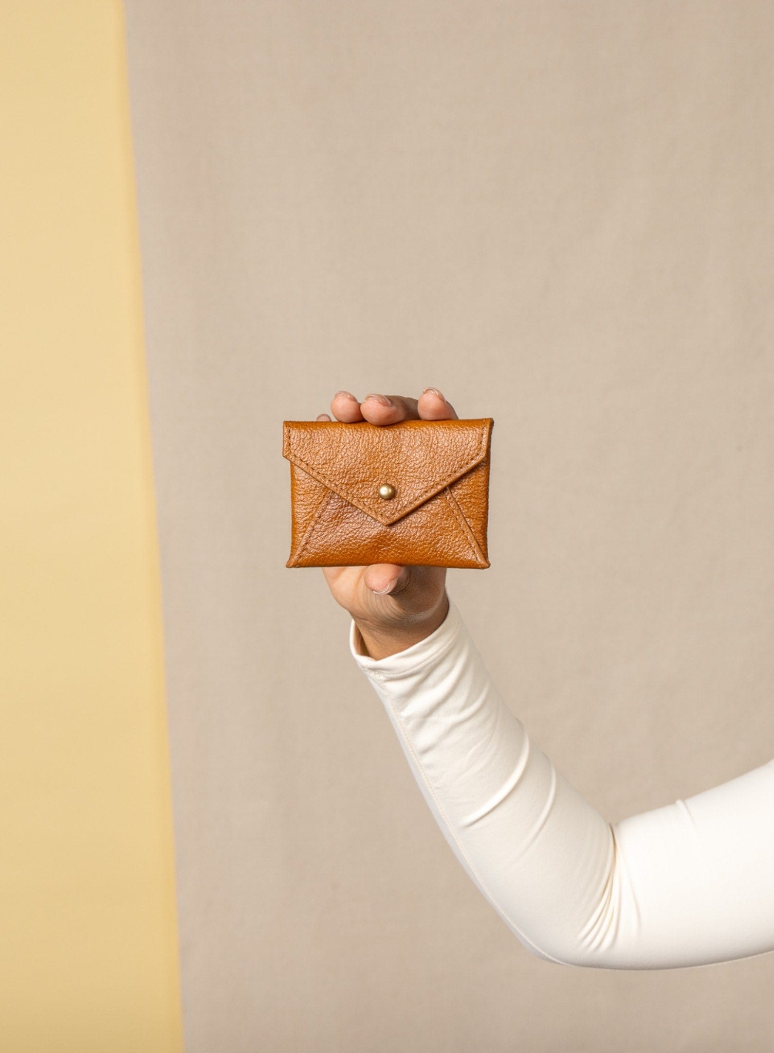 Person holding a cognac leather coin pouch against a beige background