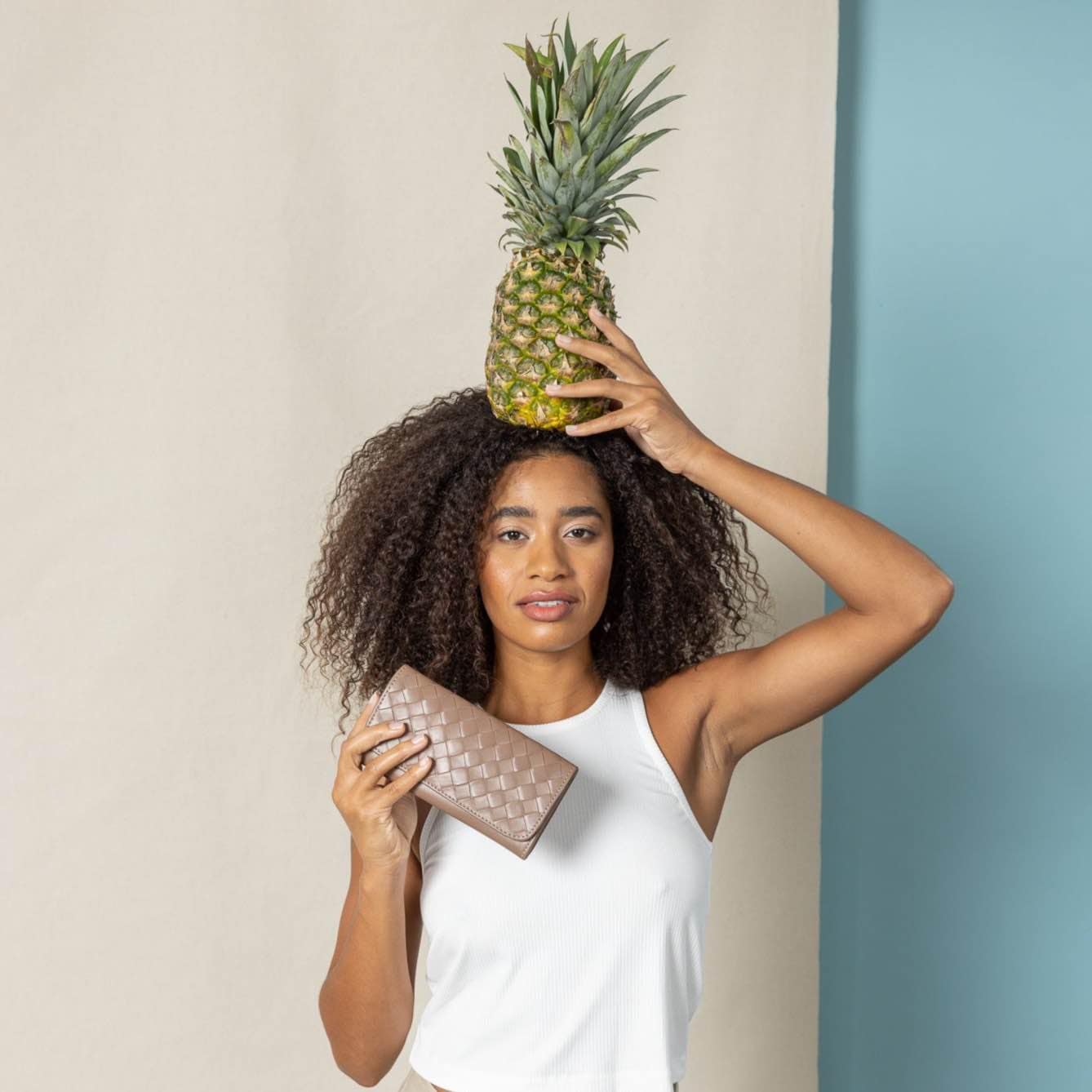 Woman holding a pineapple on her head and a trifold wallet with a neutral background