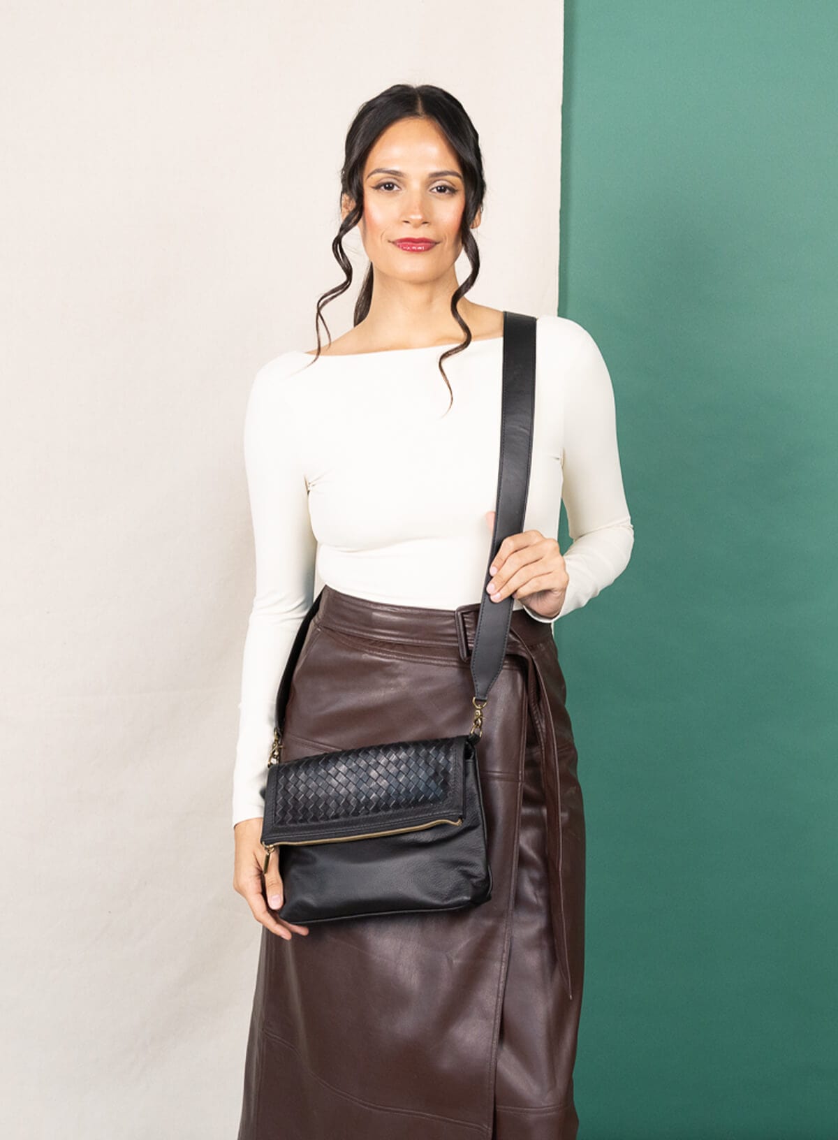 Woman holding a black handbag against a green and white background