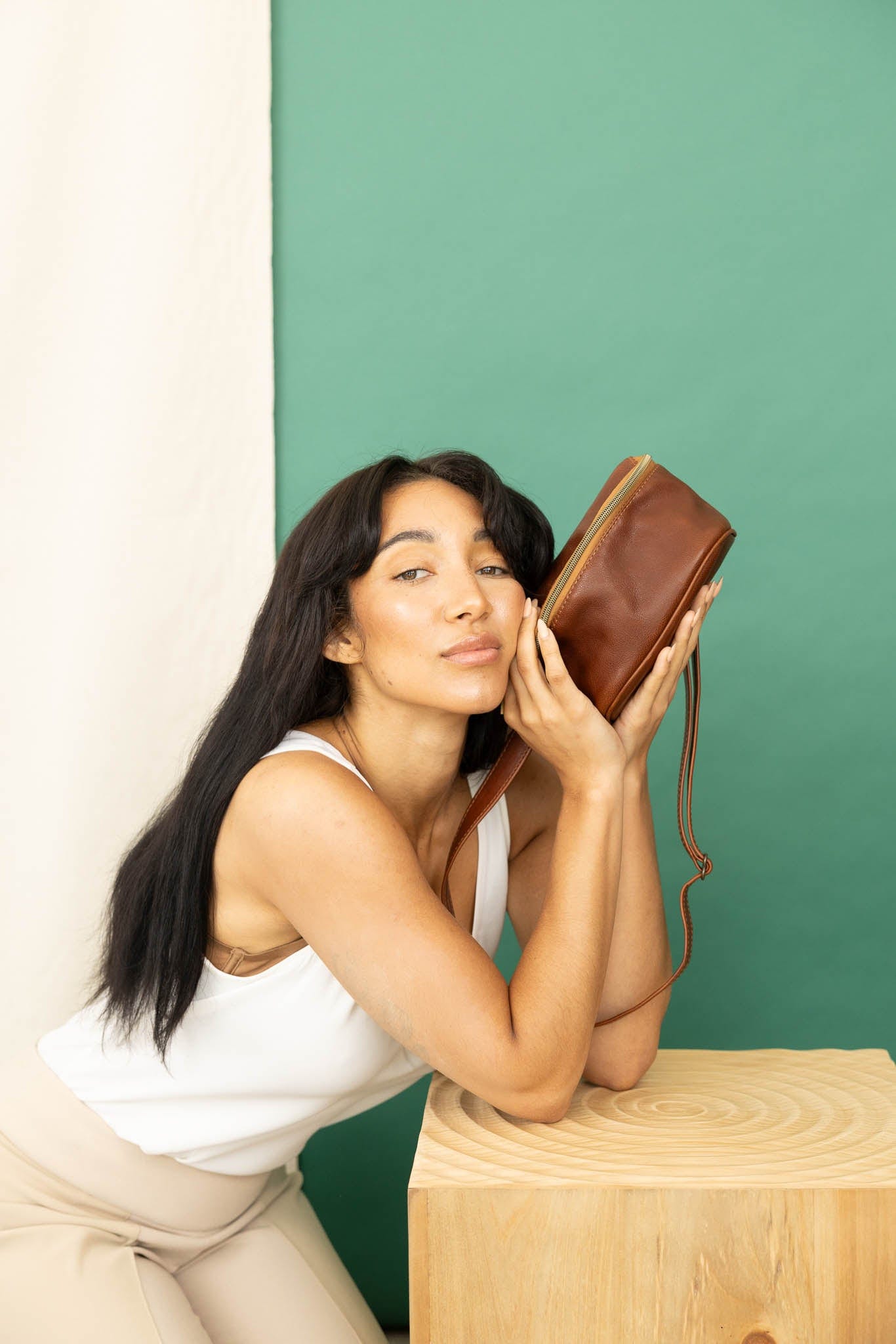 Hip bag in mahogany from the fall/winter collection held by model leaning on a table.