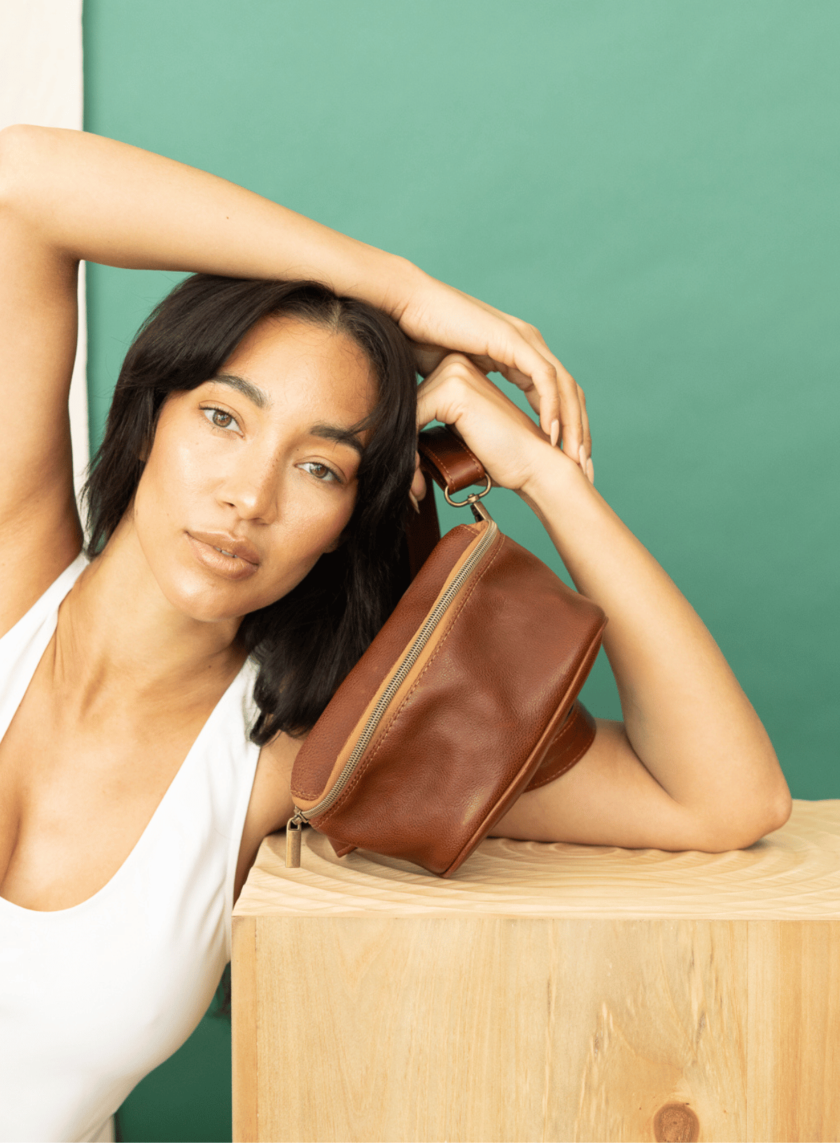 Hip bag in mahogany from the fall/winter collection held by model leaning on a table.