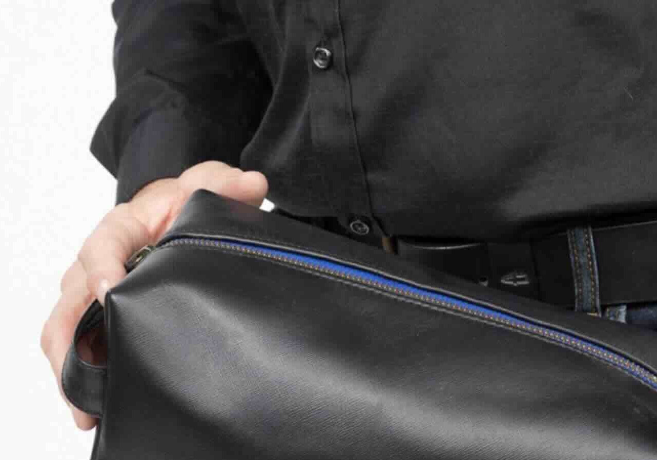 Man holding black leather toiletry bag, close-up