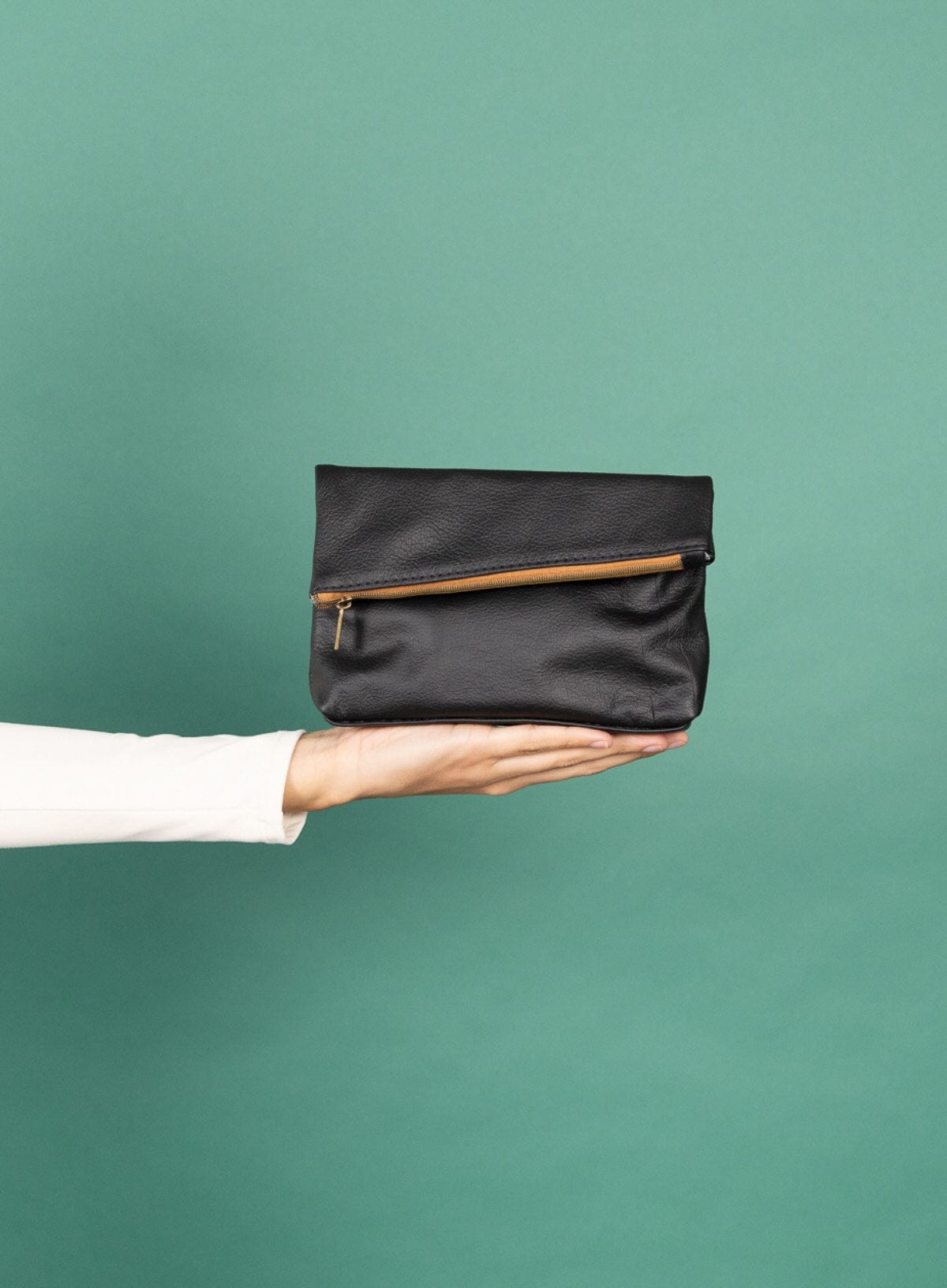 Hand holding a black makeup bag against a green background