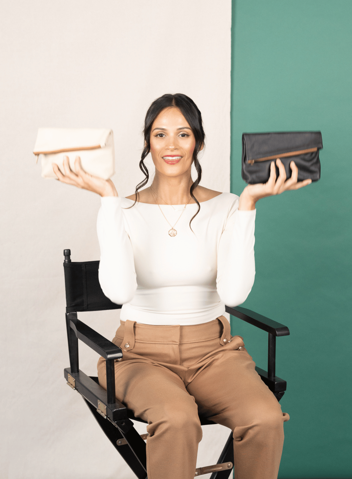women sitting on a chair holding up two makeup bags in black and bone