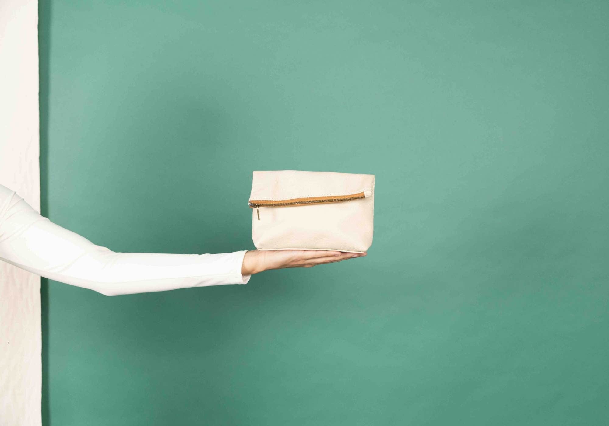 Bone-colored makeup bag held against green background