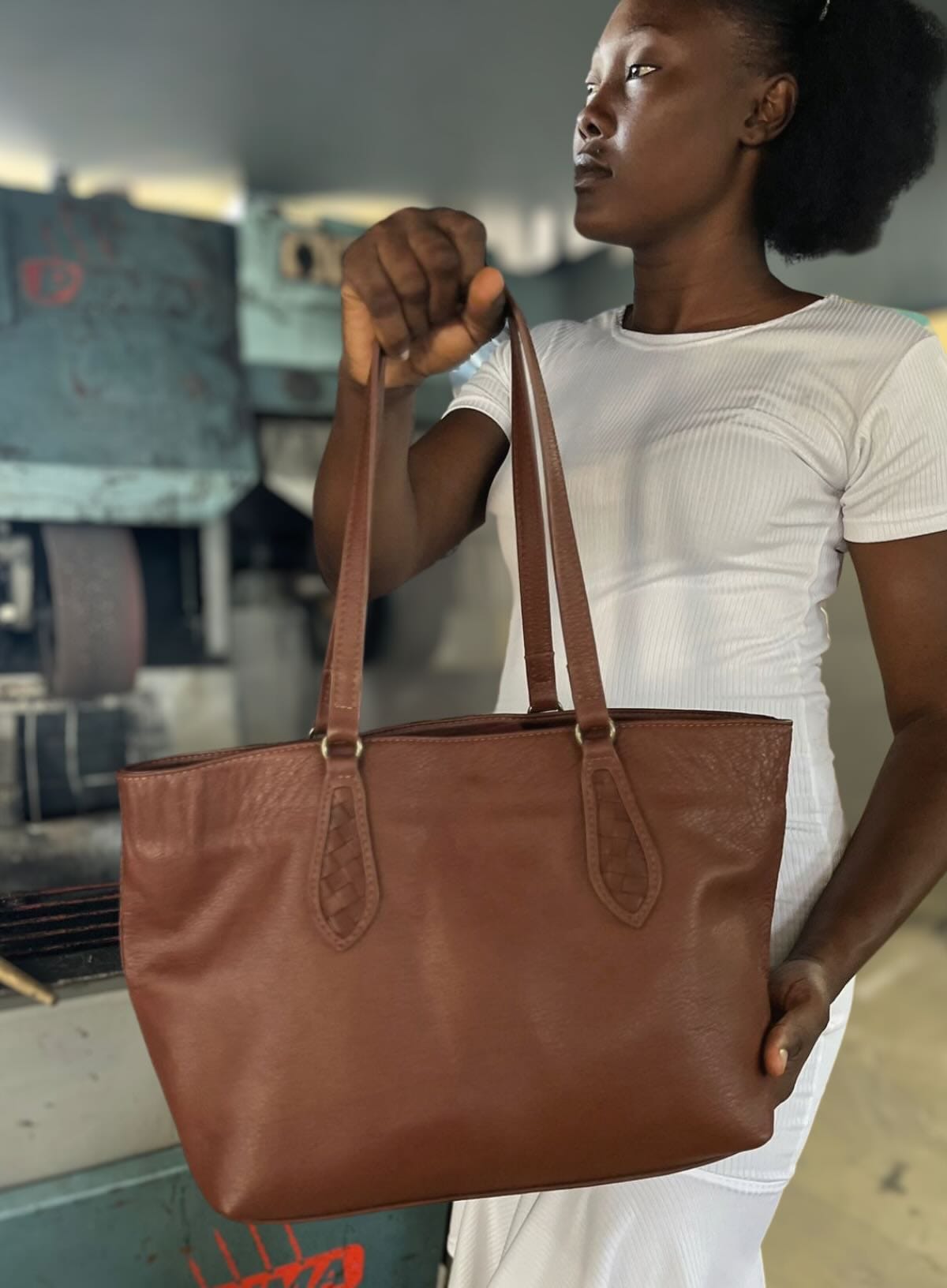 Artisan holding a brown leather tote bag in Haiti factory
