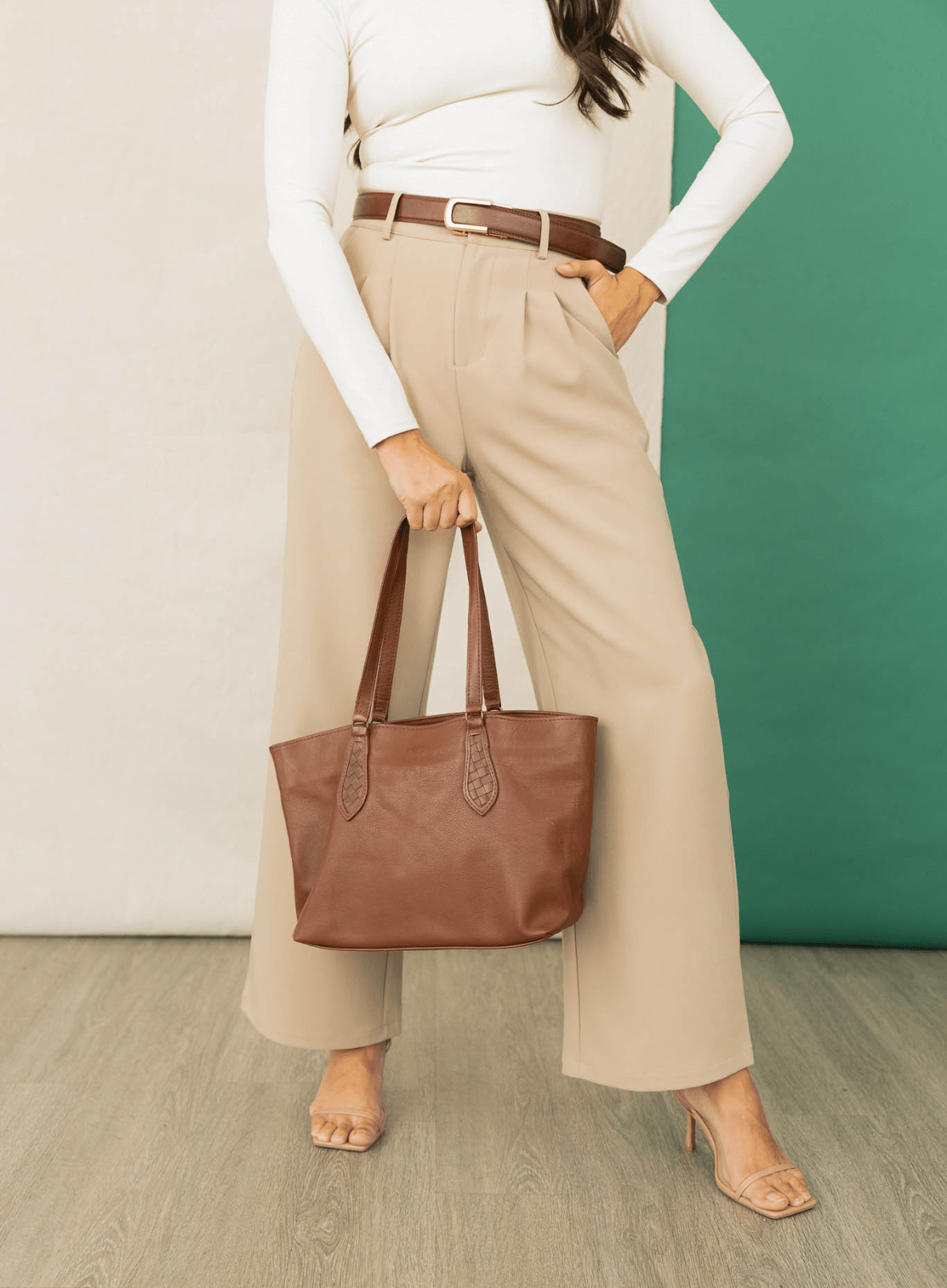 Person holding a brown leather tote bag against a green and white background