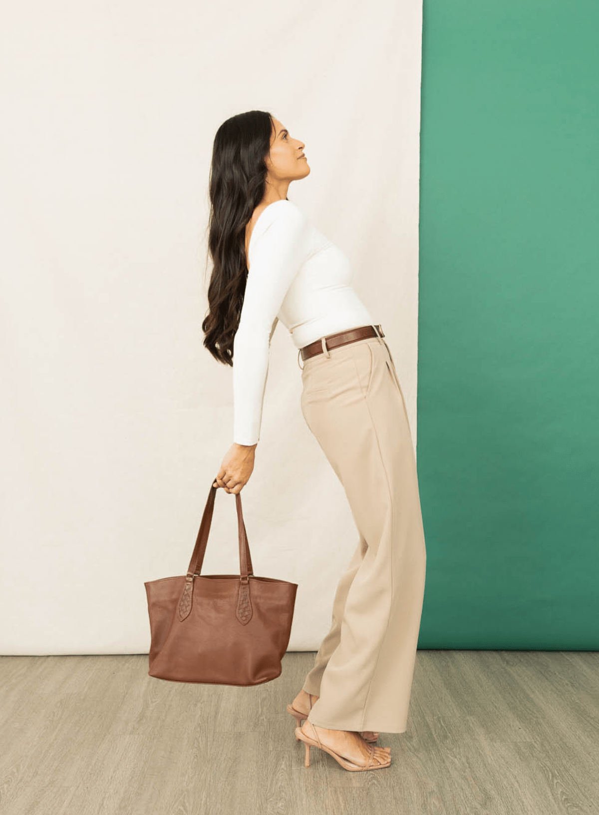 Woman holding a brown tote bag against a white and green wall.