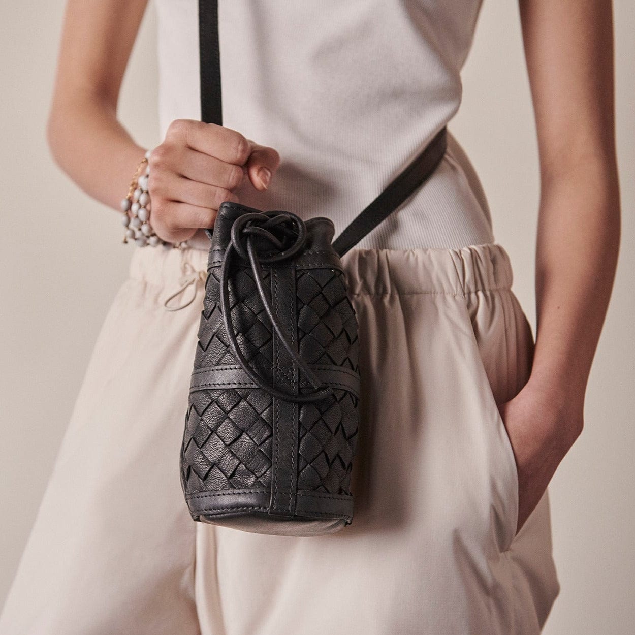 Person holding a black woven handbag against a neutral background