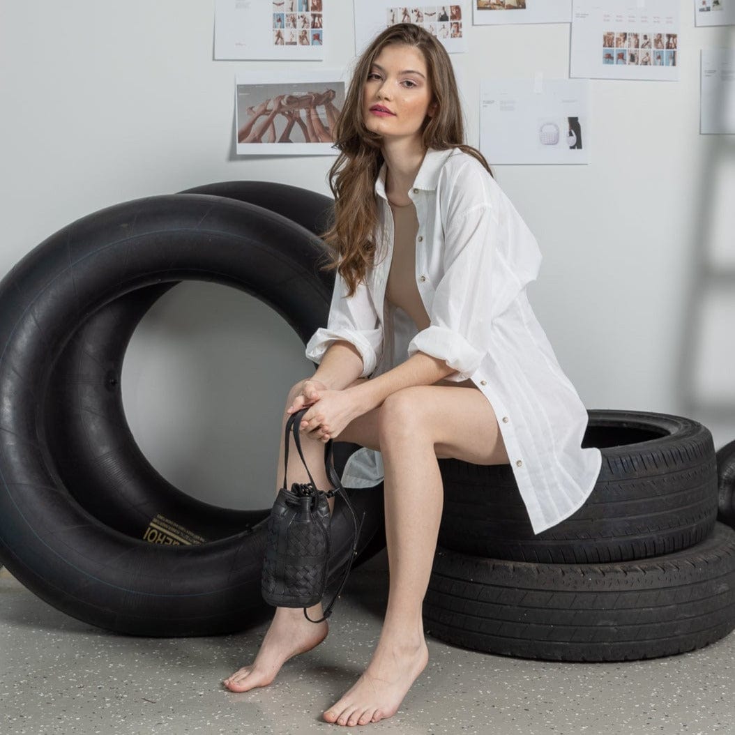 Woman holding leather bag sitting among stacked tires in a casual setting