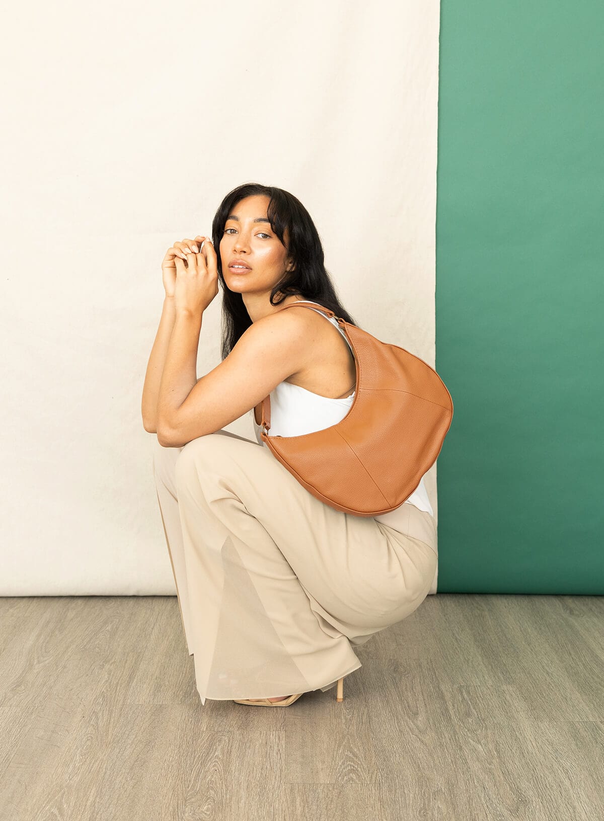 Woman holding a honey leather bag against a white and green wall.