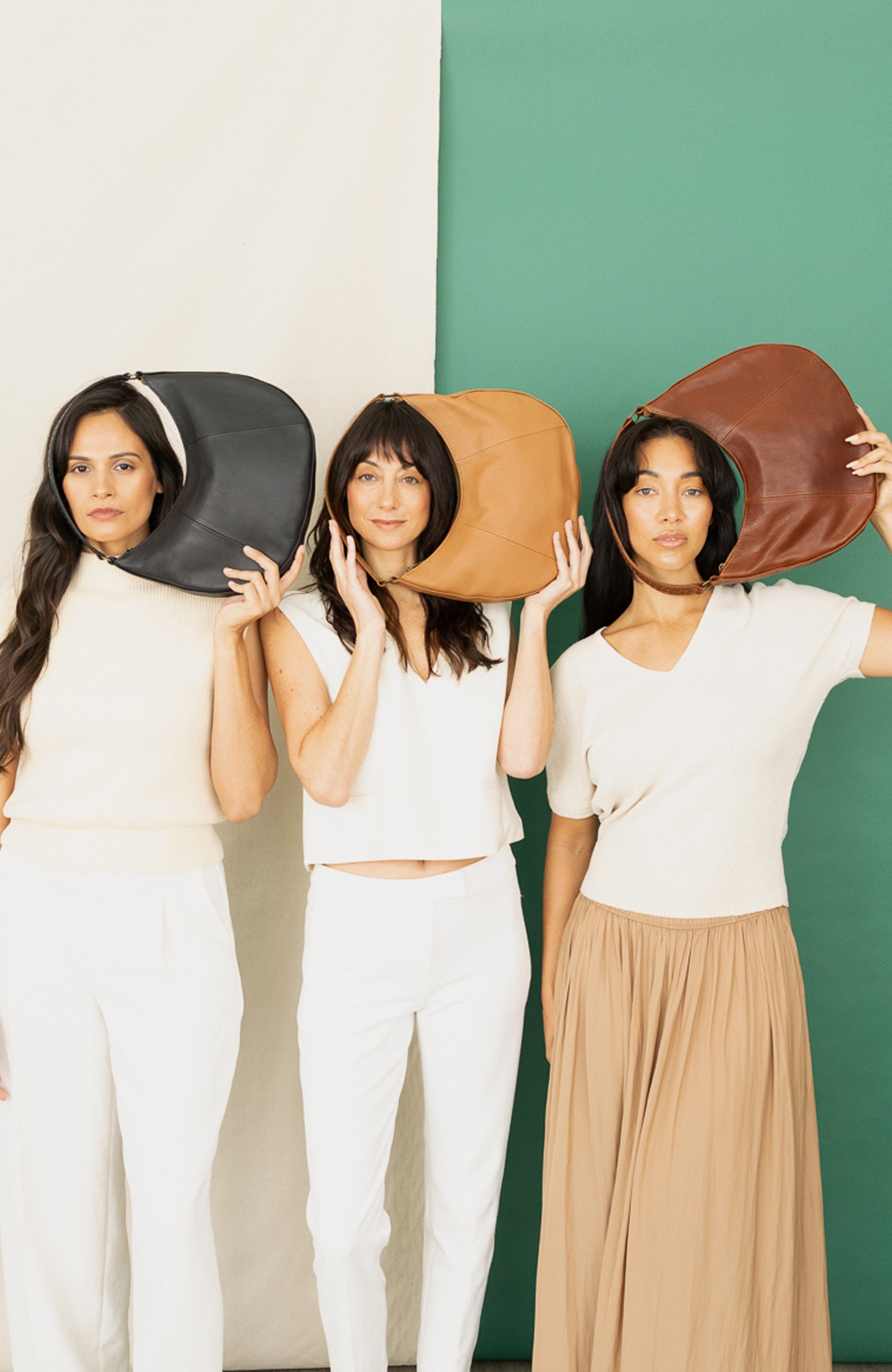 Three women holding different colored hats against a green and white background