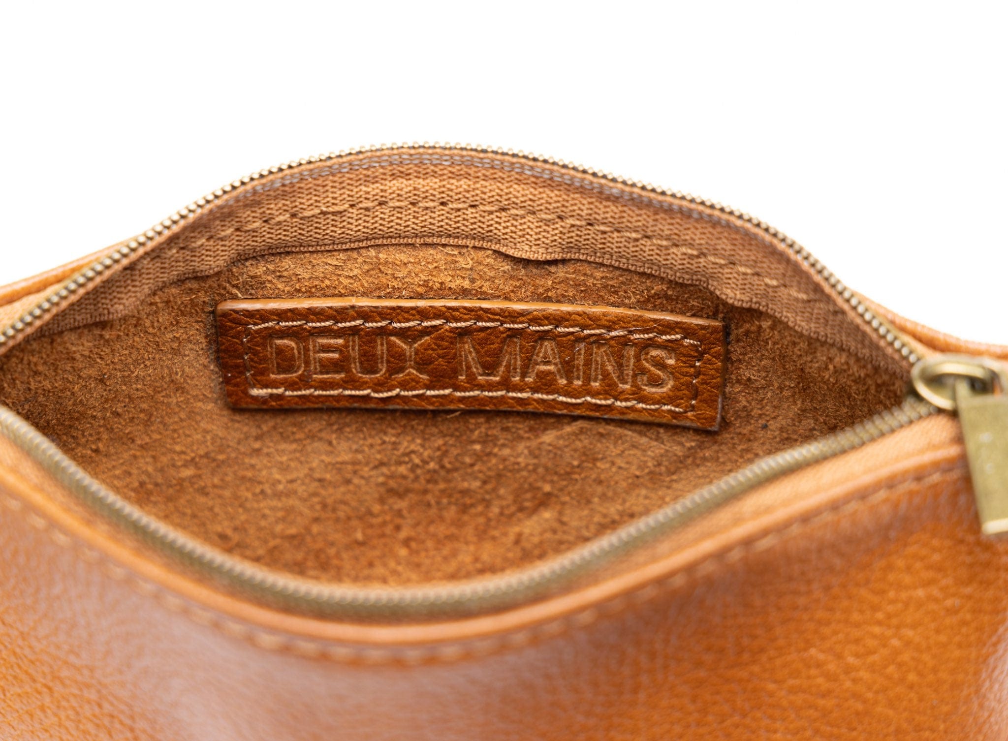 Close-up of a cognac leather pouch with 'DEUX MAINS' branding on a white background
