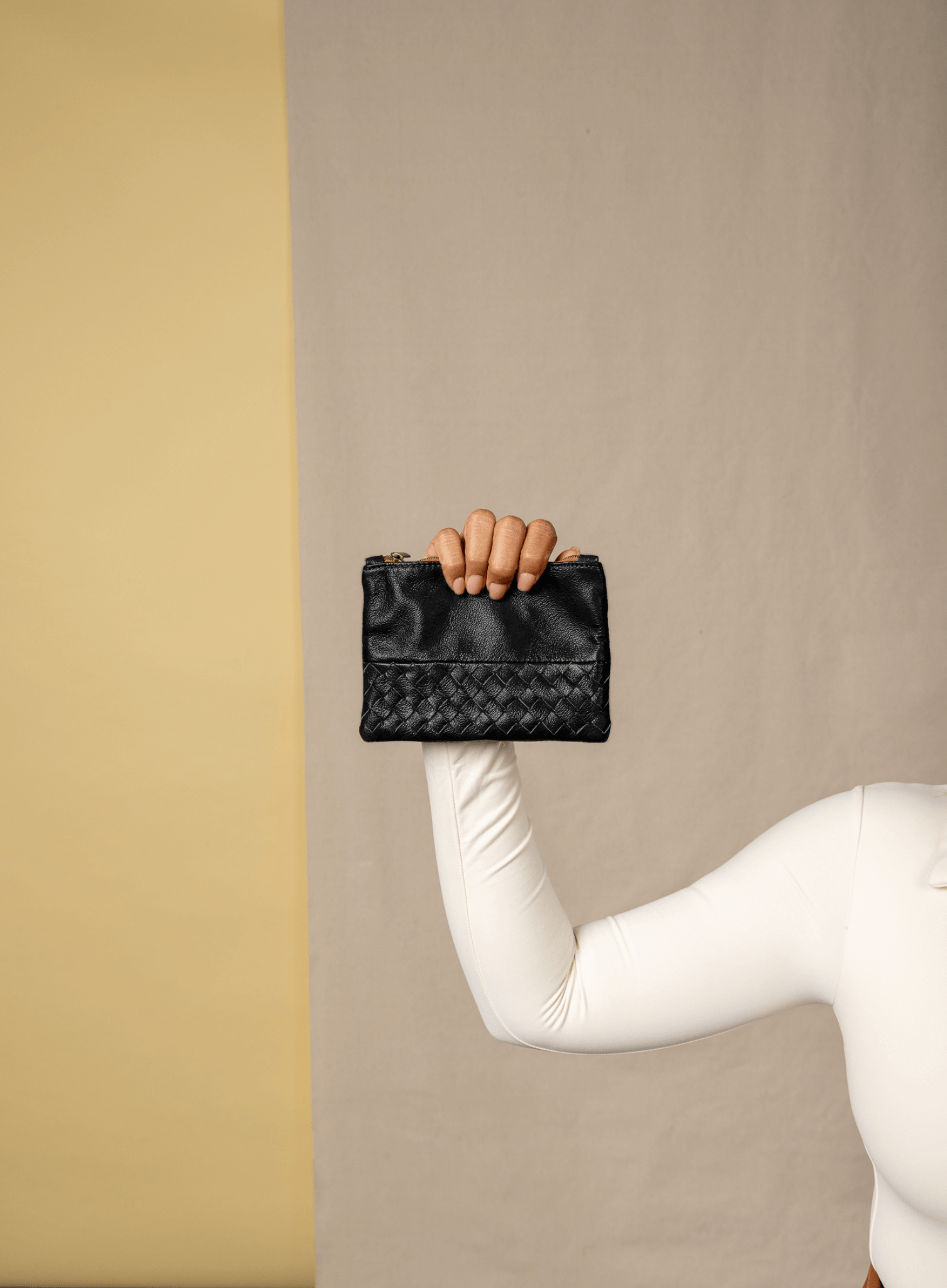 Black woven pouch held by a hand against a beige wall