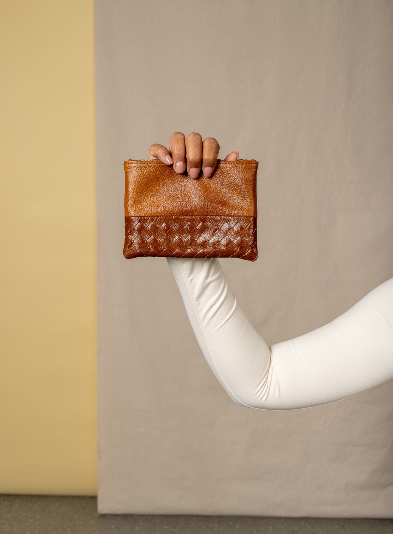 Cognac woven pouches held by a hand against a beige background