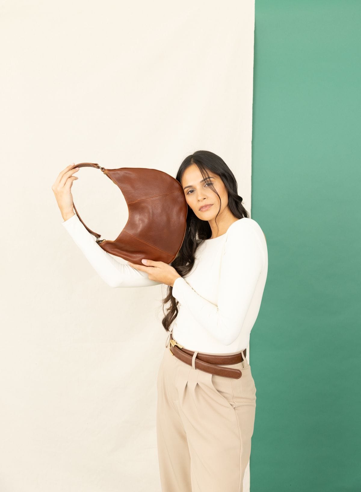 Woman holding a brown leather handbag against a green and beige background
