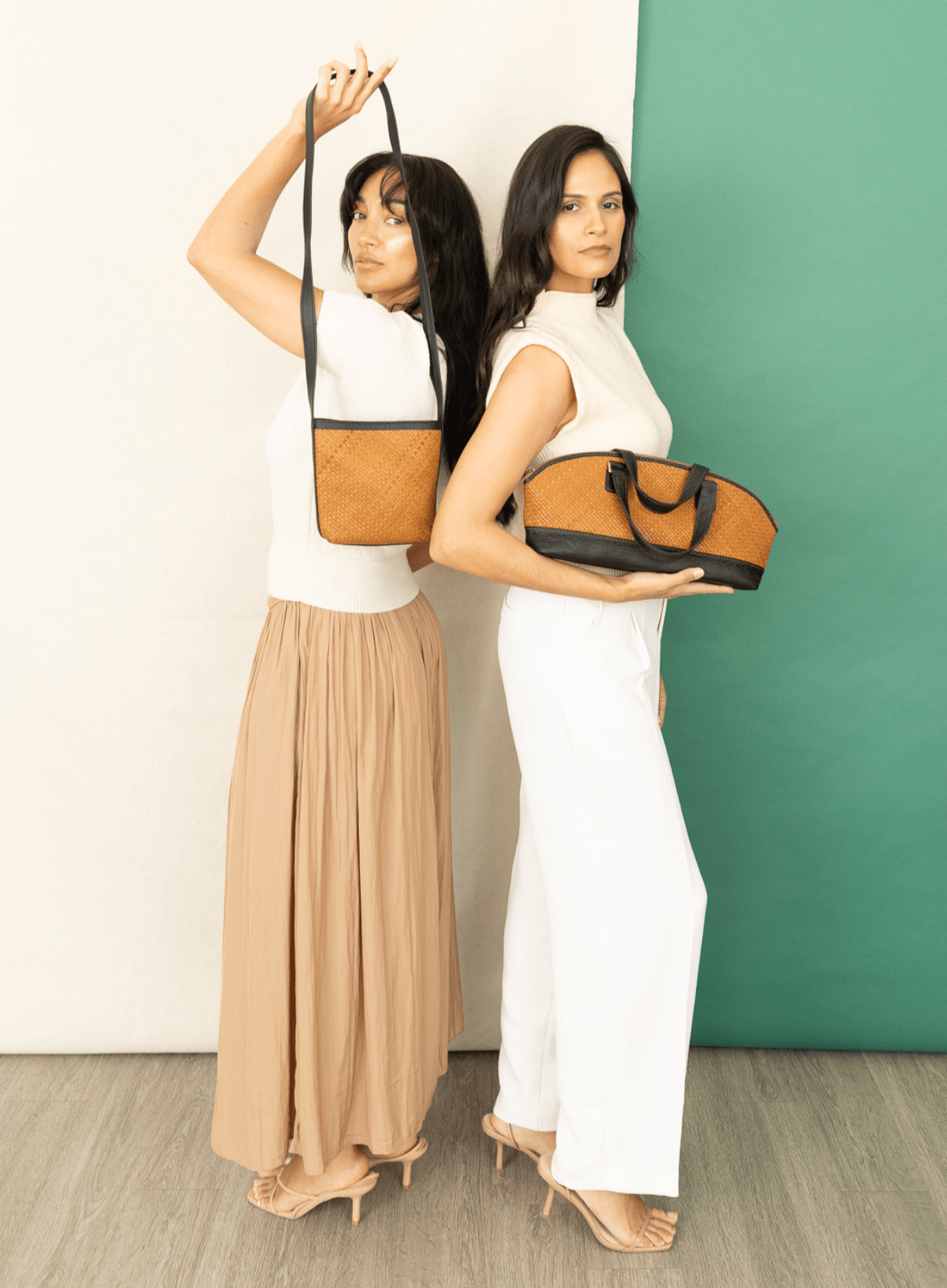 Two women holding different handbags against a white and green background