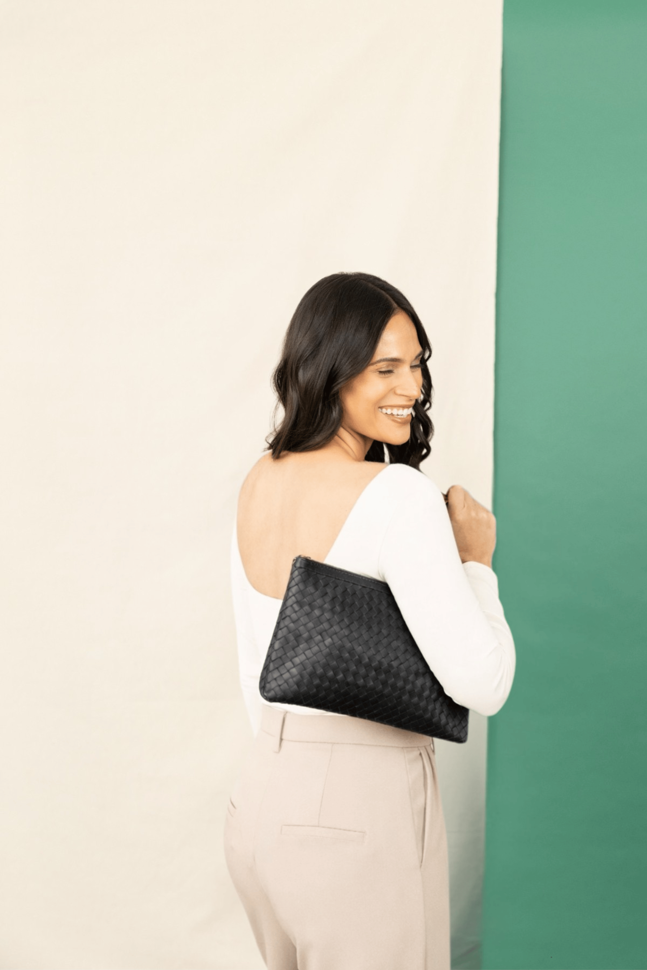 Woman holding a black clutch against a light beige and green background