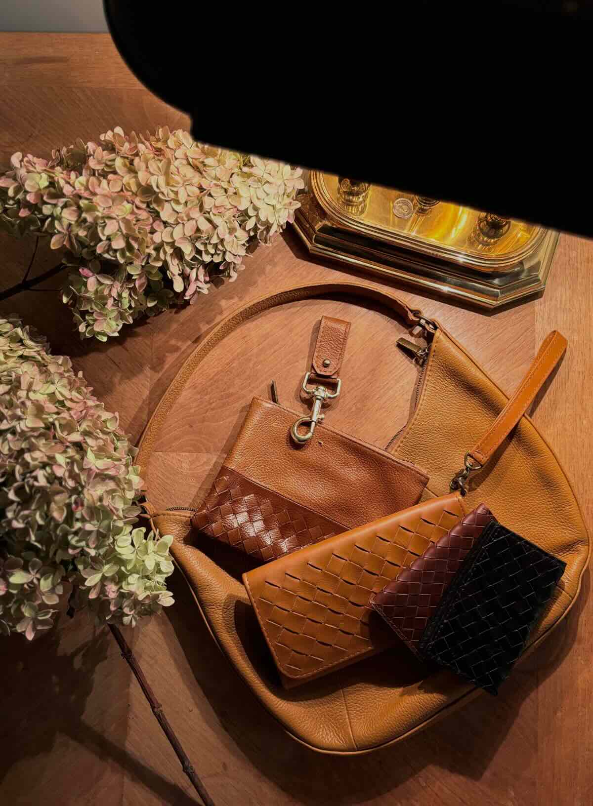 leather woven wallets with on a wooden surface with flowers and a lamp.