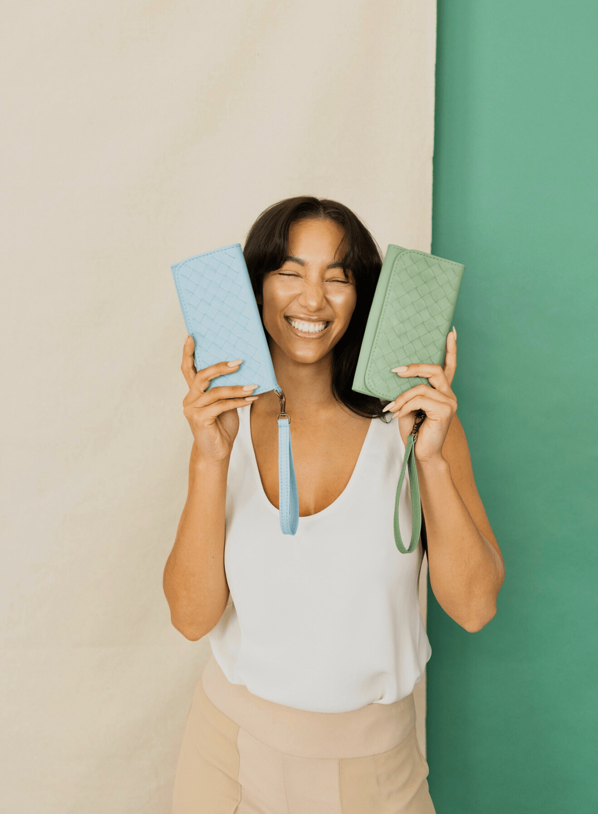 Woman holding sky blue & sage green wristlet wallets