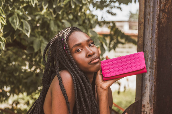 woman holding up the fuchsia wallet in nature.