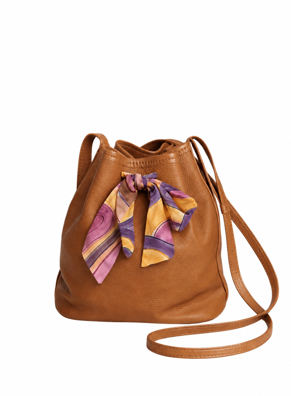A tan leather bucket bag with a matching shoulder strap and a colorful patterned silk scarf tied in a bow at the front, set against a plain white background.