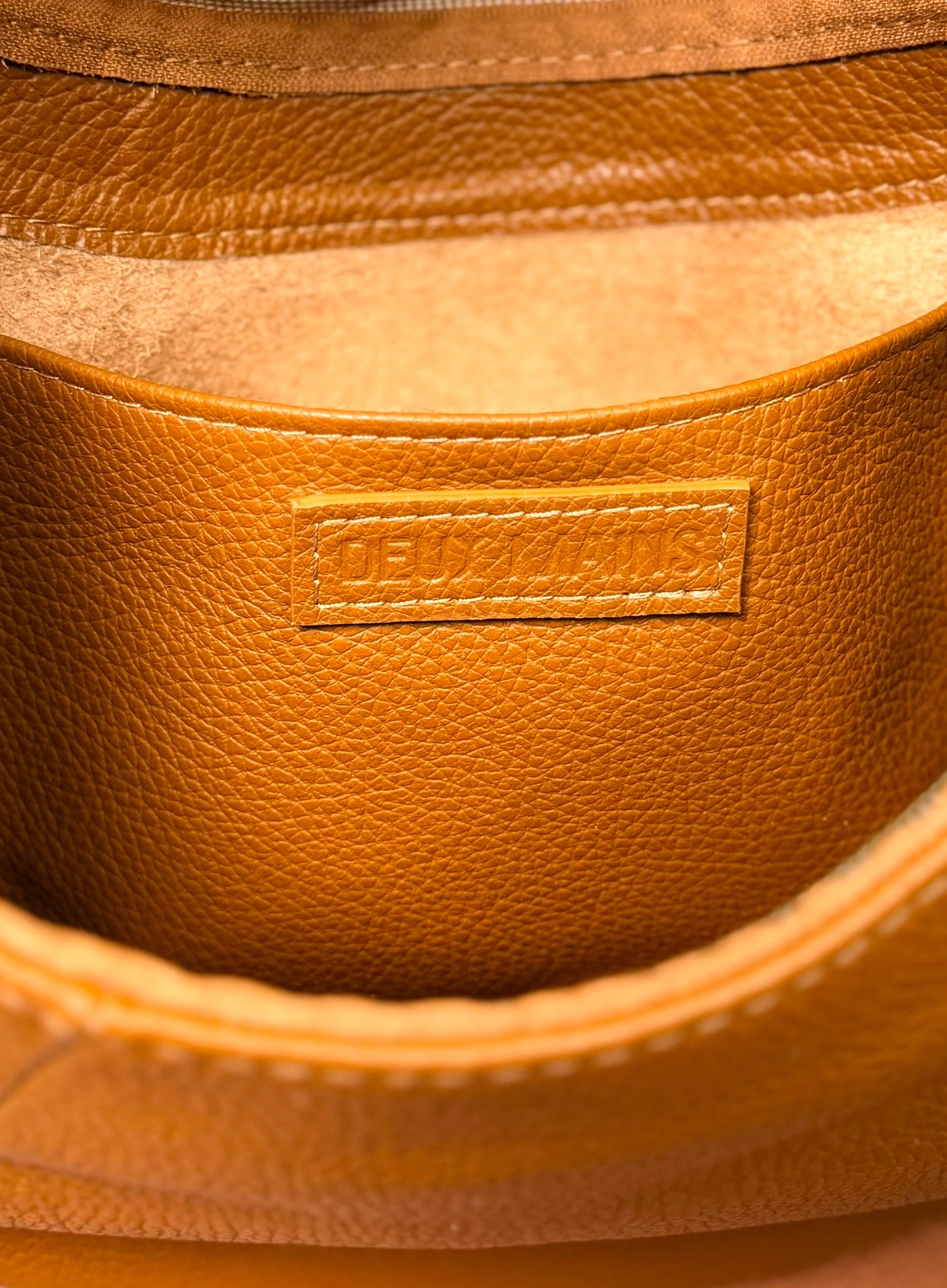 Close-up of a tan pebbled leather interior pocket with a rectangular embossed brand label reading DE VALLIERS.