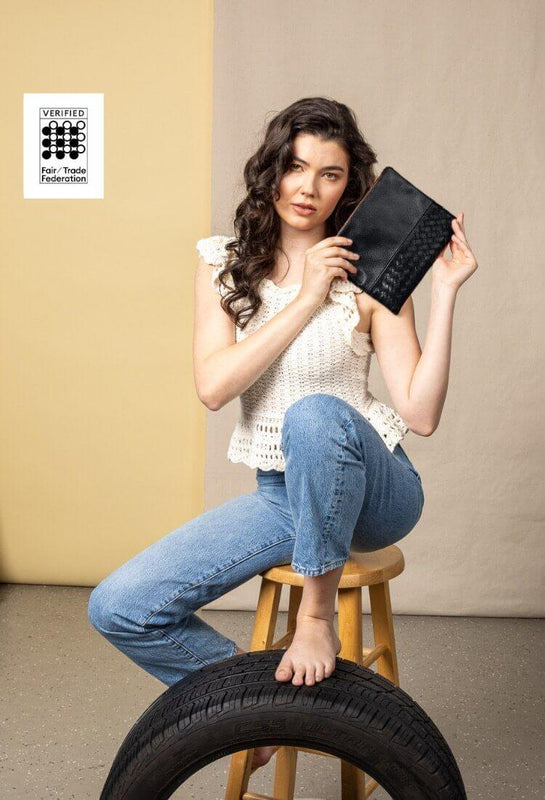 Model sitting on a stool, leaning on a wheel, holding a black large pouch from our spring collection.