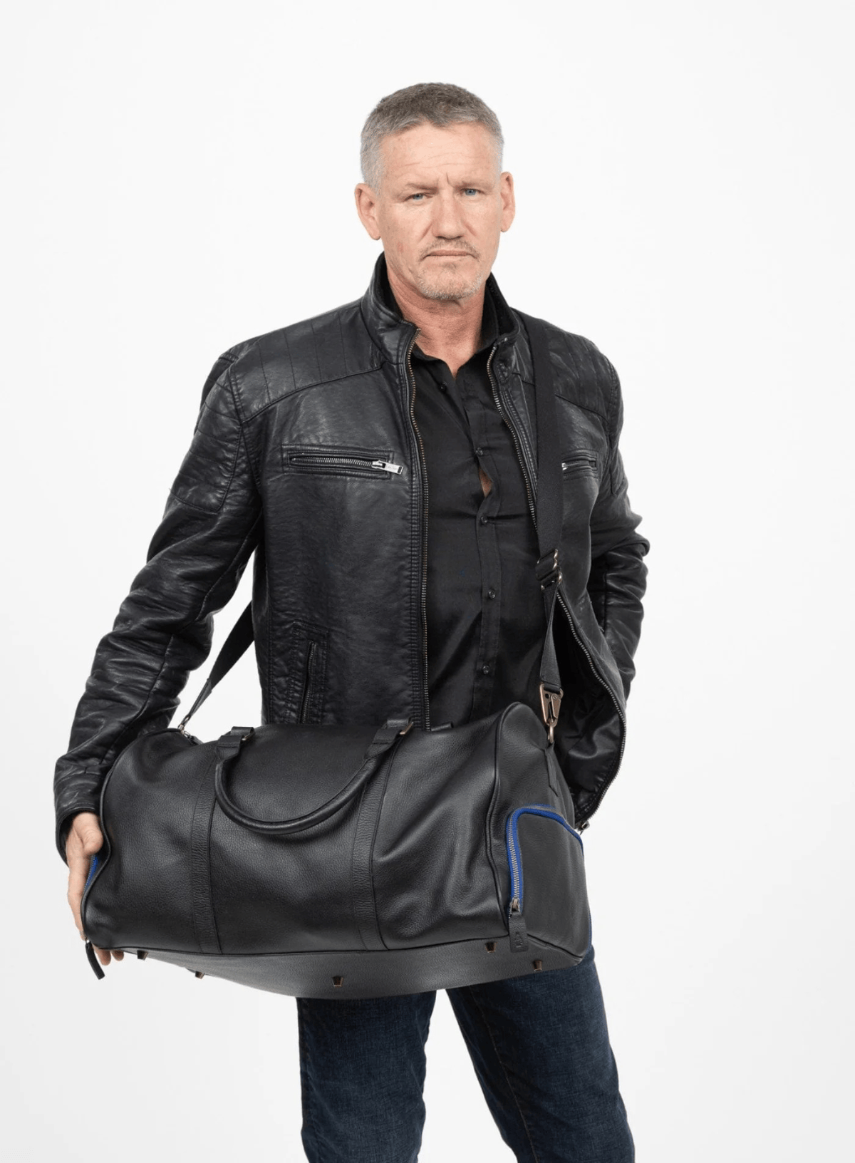 Man holding a black leather duffel bag against a white background