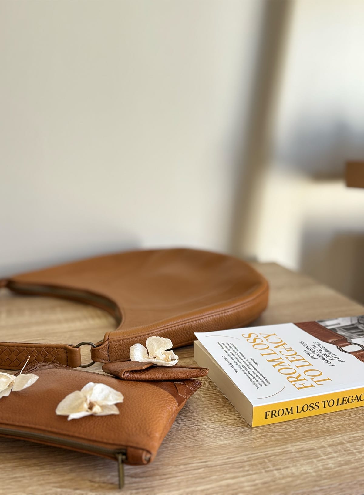 Brown leather handbag and book on a wooden surface with a blurred background