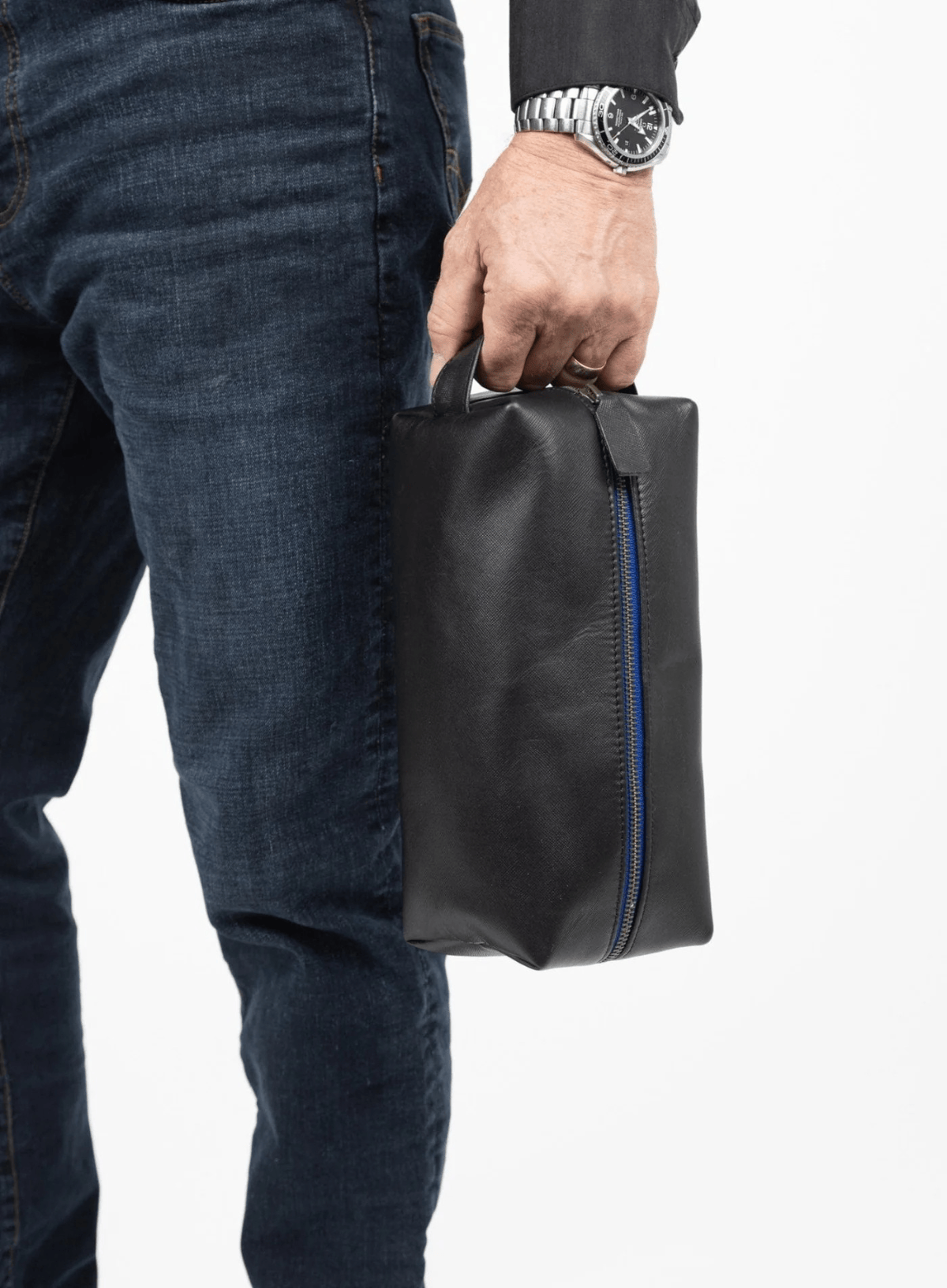 Person holding a black leather toiletry bag with a blue zipper against a white background