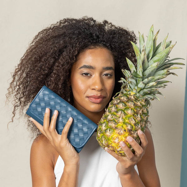 Classic Taupe Trifold Wallet showcasing side view in blue held by model with pineapple, a timeless and functional accessory for your everyday essentials.