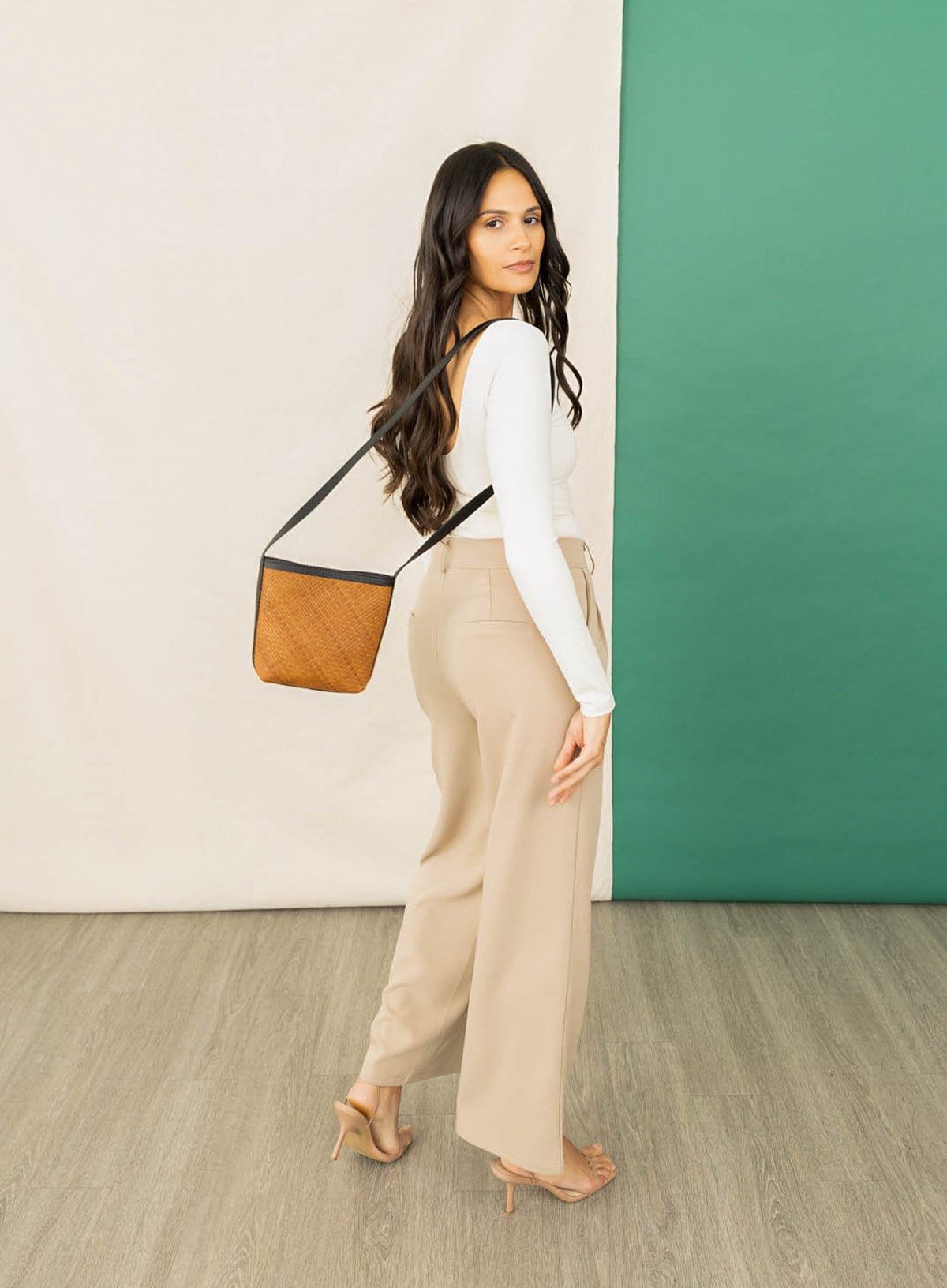 Woman holding a leather crossbody bag against a green and beige wall