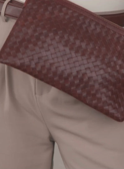woven crossbody clutch in brown held by model pulling the straps.