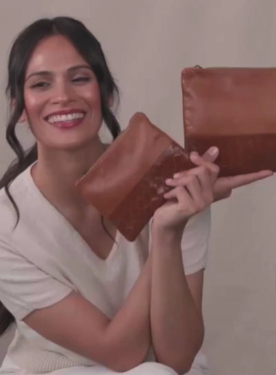 Model sitting down holding up the small and large pouches from fall/winter collection.