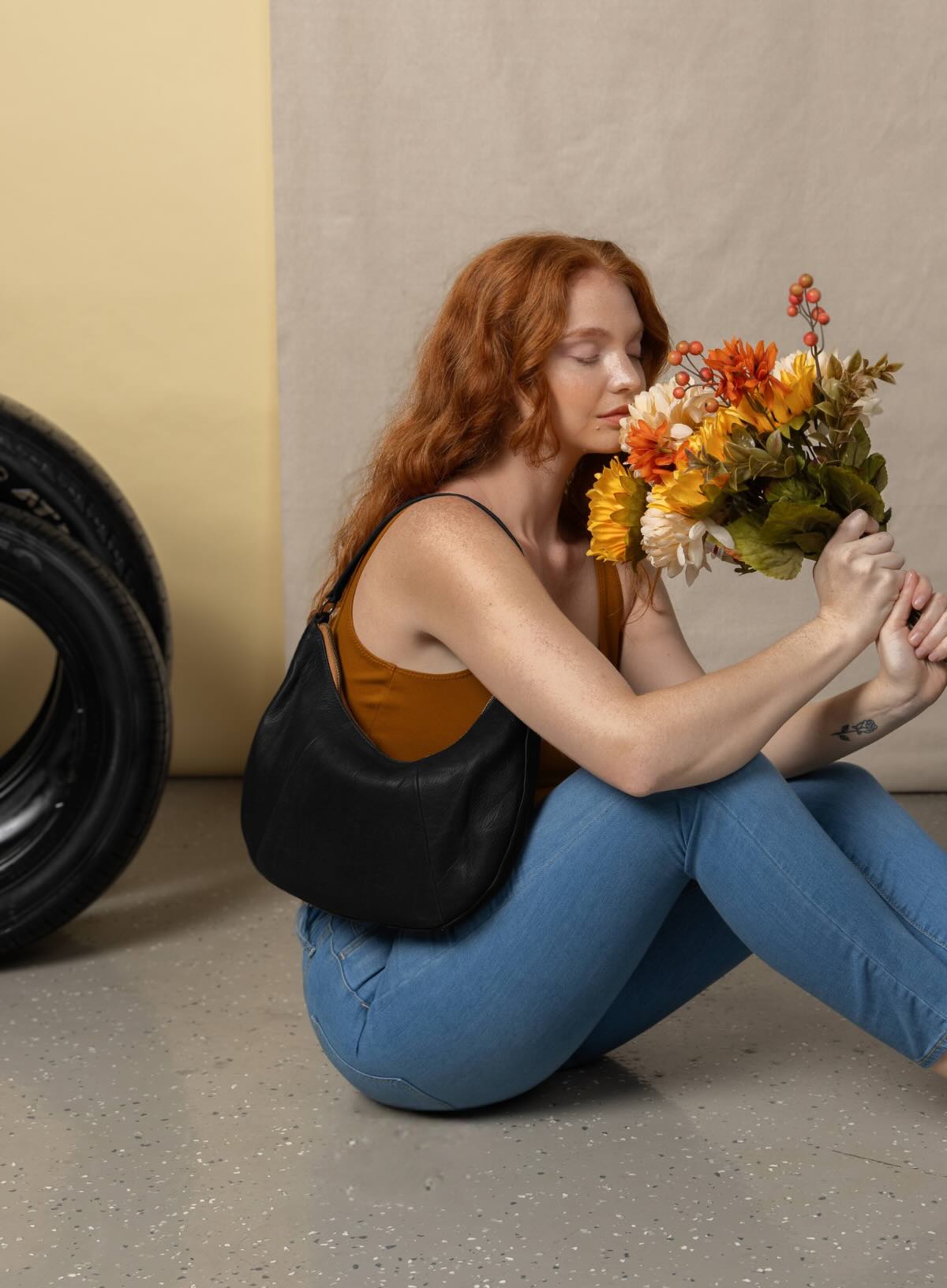 saddle shoulder bag from spring and summer collection in black held by model sitting holding flowers.