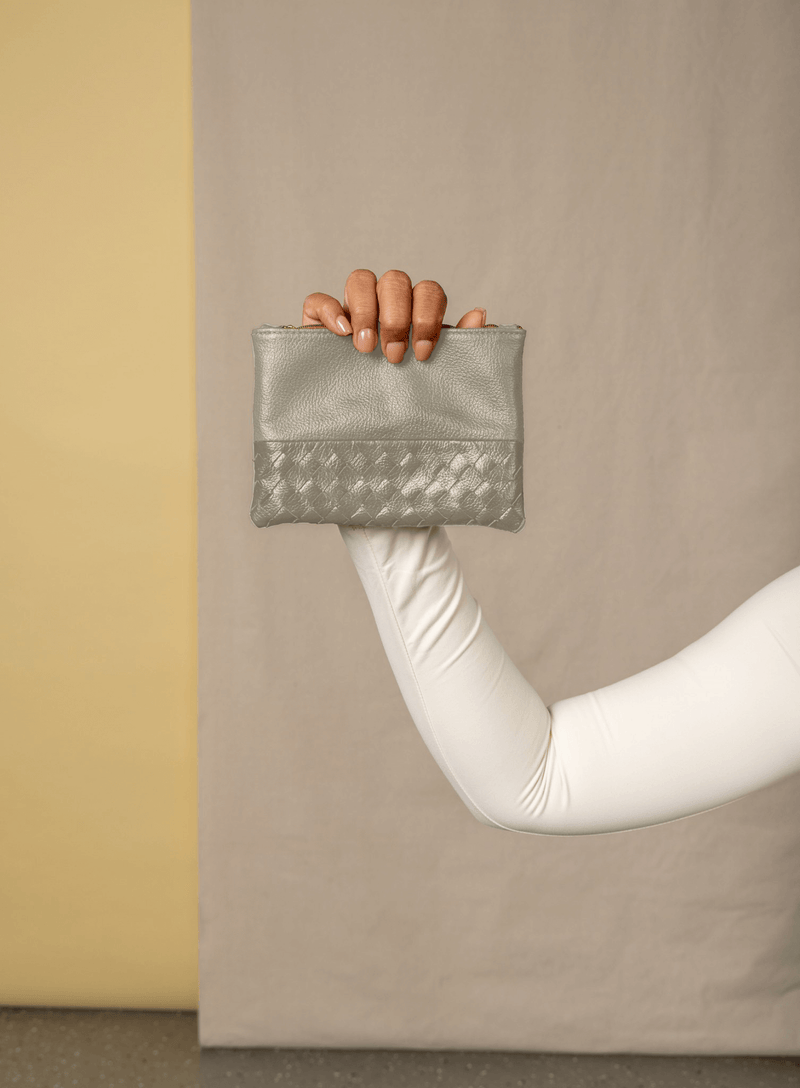 smalll pouch from sustainably hand made accessories in bone held by model showcasing front view.