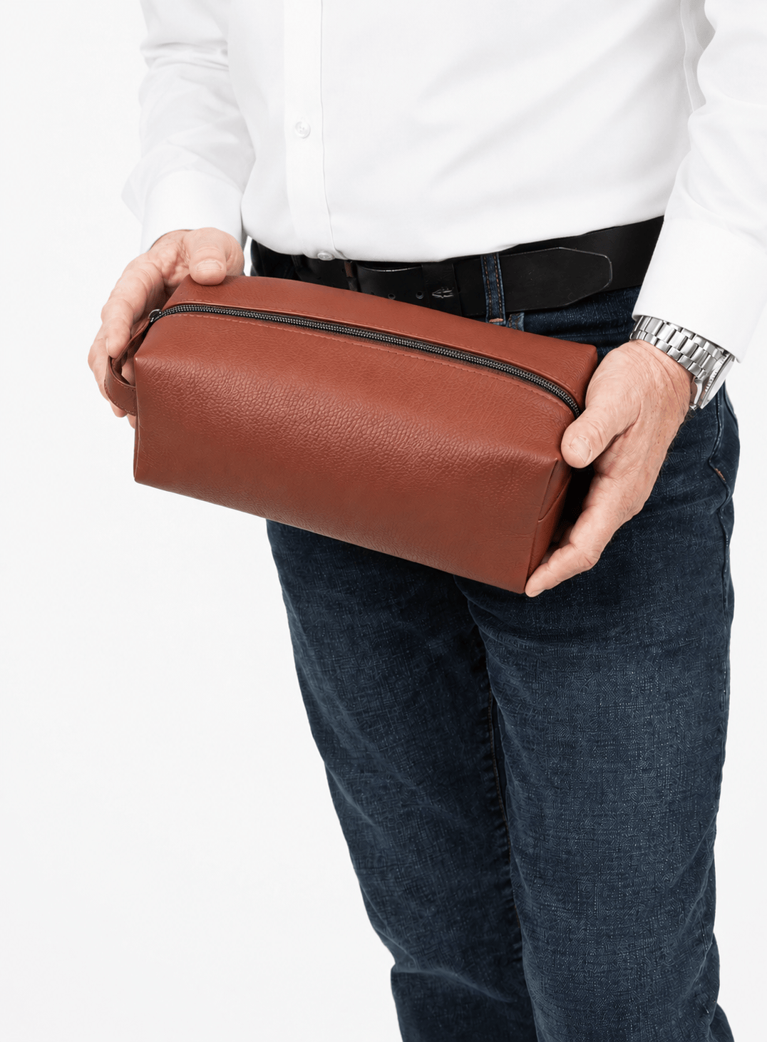 Person holding a brown leather dopp kit against a white background