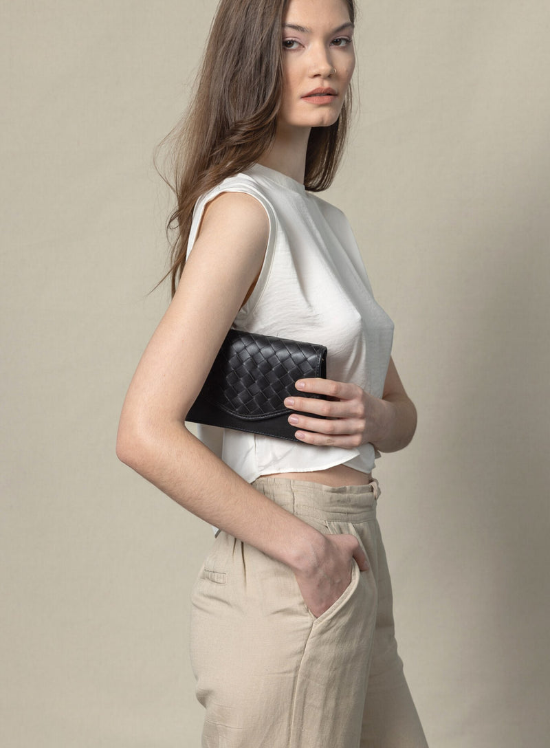 woven belt bag in black from womens bags collection with model showcasing it held underneath arm.