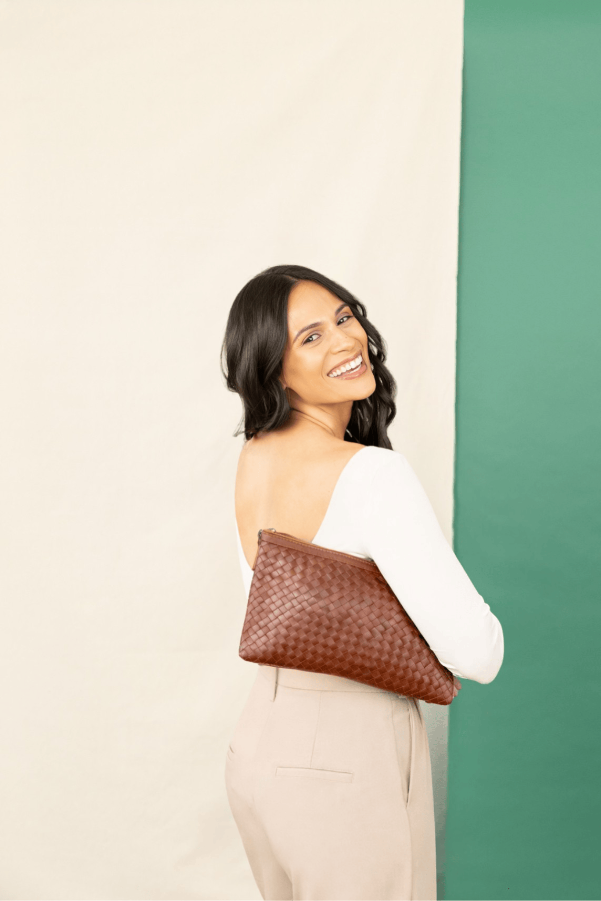 Woman holding a brown clutch against a green and beige wall