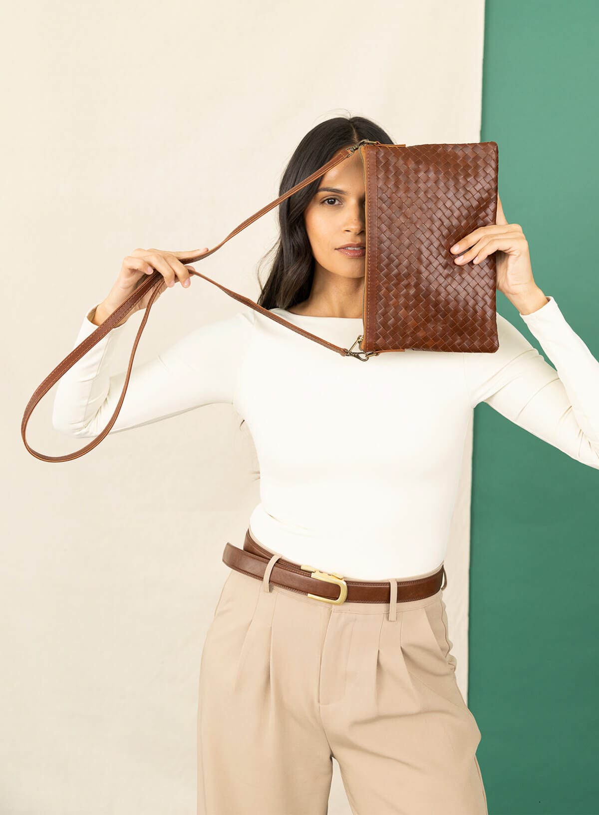 woven crossbody bag held by model hiding.